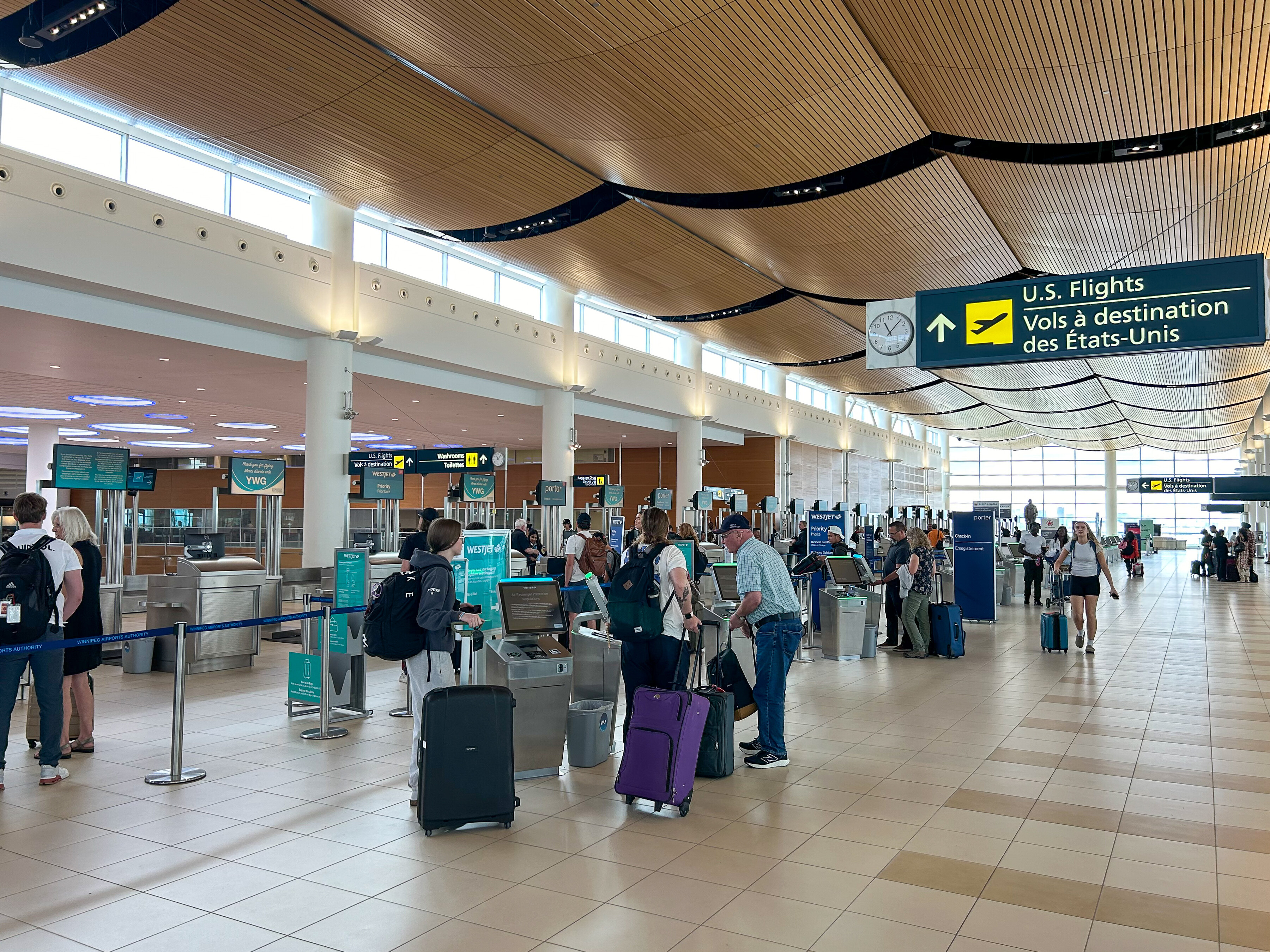 Passengers gather around the check-in kiosks on the Departures Level of the Winnipeg Richardson International Airport terminal